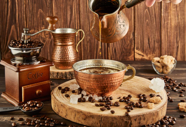 istock Pouring coffee from coffee maker into copper cup, an antique coffee grinder and copper milk jug on wooden background 2142568912