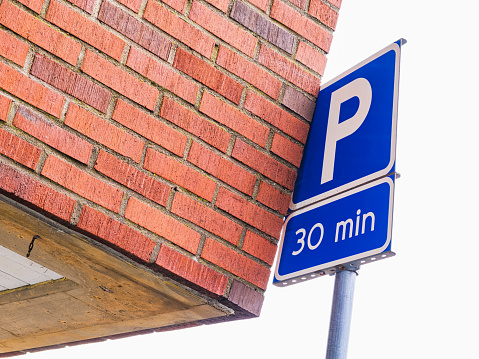 A blue parking sign is prominently displayed next to a red brick building in an urban setting. The sign indicates parking regulations and restrictions for the area.