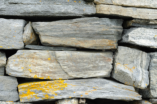 A detailed view of a dry stone wall with interlocking gray stones and patches of yellow lichen.