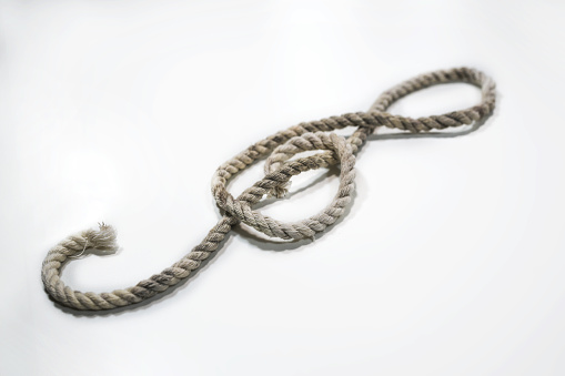 Old rough rope laying in the shape of a treble clef or violin key on a light gray background, musical symbol, copy space, selected focus, narrow depth of field