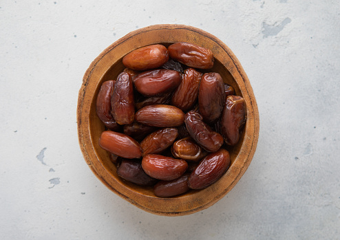 Wooden bowl of dried sweet brown dates on light background.