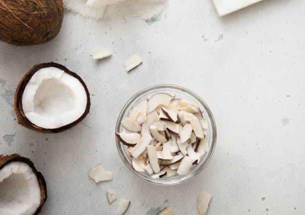 Dried sweet coconut slices chips in glass bowl on light background.Top view. stock photo