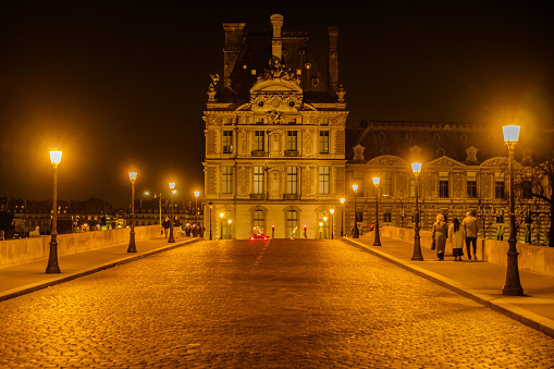 Paris, France - February 17, 2024 : View of the illuminated Pont Royal with beautiful streetlights and part of the Louvre Museum in the background in Paris France