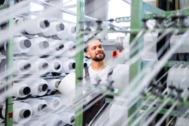 istock Experienced textile factory worker changing thread spool on industrial knitting machine. 2142669597