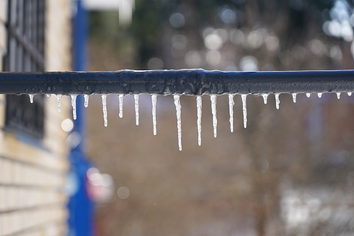 Several icicles of varying lengths hang from the gray pipe of the crossbar. A country landscape is visible in the background. Background.