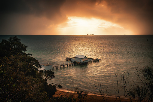 The sunrise view of a pier in Millionaire's Walk in Mornington Peninsula with a ship sailing in the sunlight in the distance