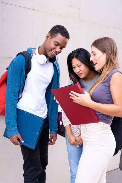 istock Smiling multiracial college student friends looking at notes, talking and laughing on campus.Vertical 2142780691