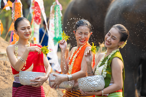 Songkran festival. Northern Thai people in Traditional clothes dressing splashing water together in Songkran day cultural festival with sand pagoda and colorful paper flag.