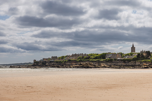 At the water edge of St Andrews, the golden beach stretches into the distance, leading eyes towards the town silhouette against a moody sky