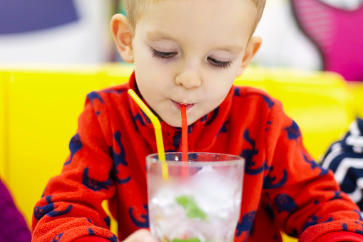 Little boy sipping water with mint leaves through a straw from a clear glass. Healthy drink and nutrition concept. Design for banner, invitation, or educational material with copy space.