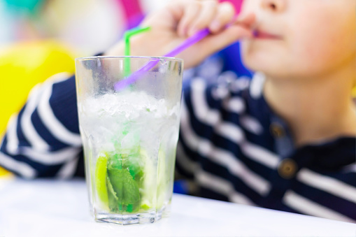 Child sipping lemonade from glass with straw. Blurred background with bokeh effect. Leisure and refreshment concept. Design for poster, banner, advertisement.
