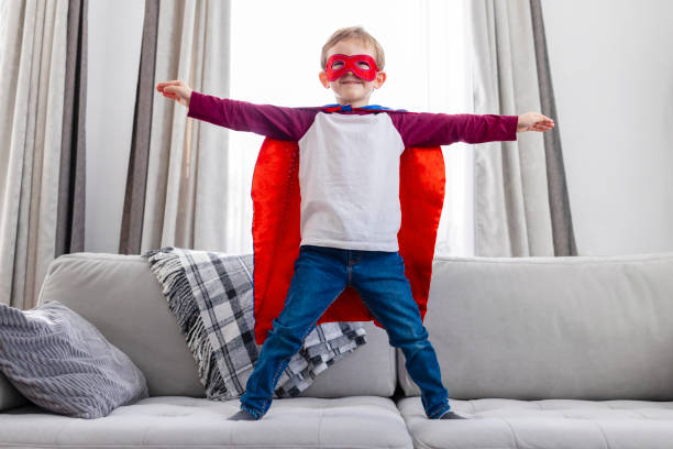 istock Child in superhero outfit standing confidently on sofa. 2142947439