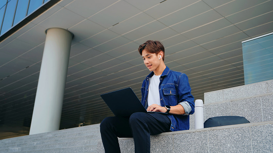 A young male professional works intently on a laptop while sitting on outdoor steps, highlighting flexibility and mobility in modern work life.