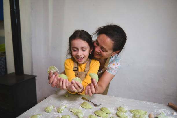 Mom and daughter have fun while cooking dumplings, standing together at floured kitchen table