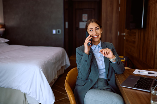Happy businesswoman making a phone call in hotel room. Copy space.