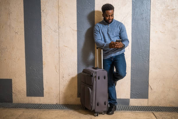 istock Man with suitcase using phone while leaning against a  wall in  passage of the railway station 2143078925