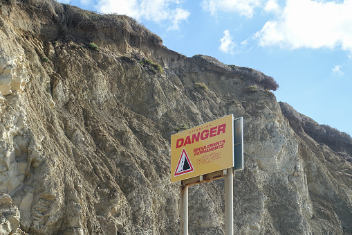 A sign warning of danger on a beach, due to a rock slide on the Basque coast