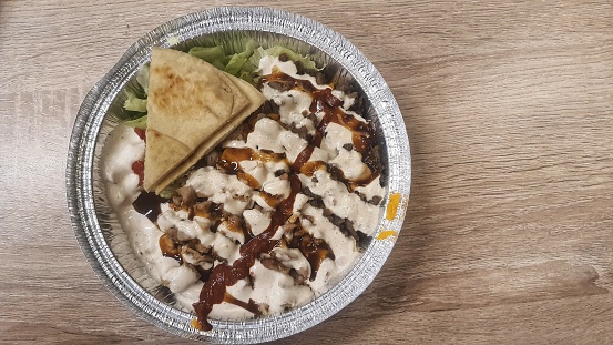 Savory grilled chicken shawarma bowl with creamy garlic sauce, drizzled with tangy sauce, accompanied by a warm pita bread.