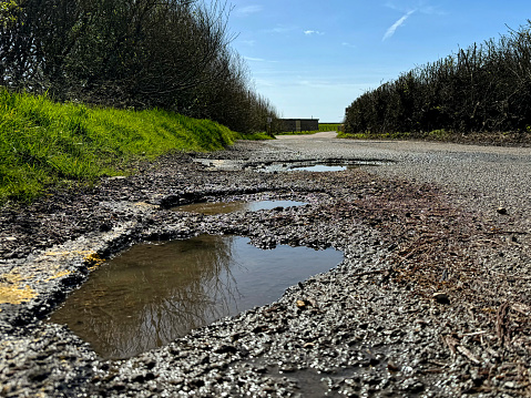 Water-filled potholes on a road near Pevensey, East Sussex, UK.