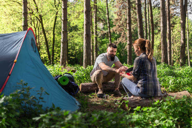 istock Happy Couple Sharing a Meal by Tent in Forest 2143207624