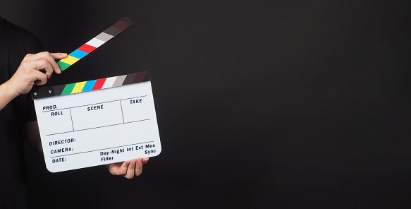 Man is holding a clapper board or slate on black background.