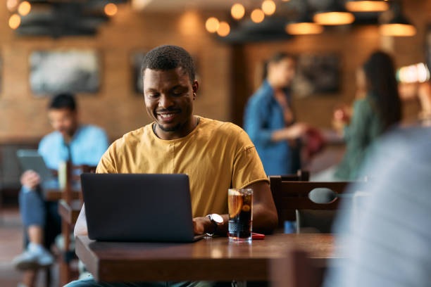 istock Happy black man surfing the net on laptop in a pub. 2143278160