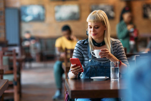 istock Smiling woman texting on cell phone while drinking coffee in a cafe. 2143278177