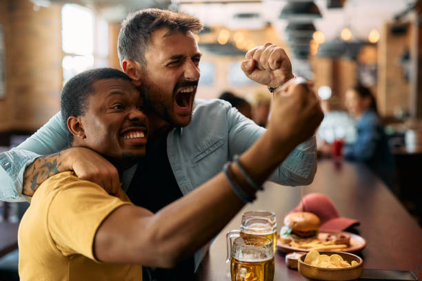 istock Excited men cheering while watching watching sports game on TV in a bar 2143280304
