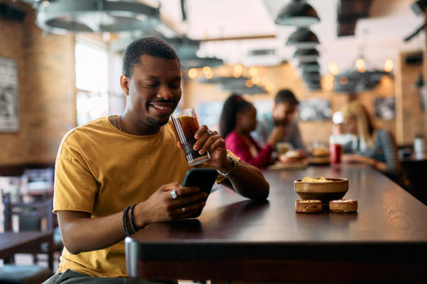 istock Happy black man using mobile phone while having a drink in a bar. 2143280830
