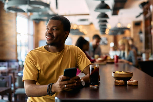istock Smiling black man text messaging on cell phone in a pub. 2143280857