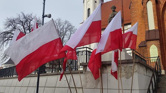 Poland flags flutter in the wind against the backdrop of a Catholic church and statue of a Catholic saint