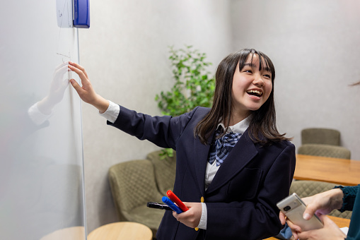 Teenage girl in uniform using whiteboard to prove math theory with teacher