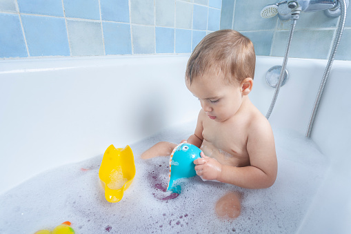 Child happily splashes in the bathtub, enchanted by a toy whale, sparking imagination and joy.