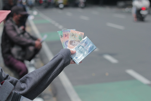 Bandung, Indonesia April 6 2024 : Asian woman hand holding a bundle of rupiah banknotes on the side of the road, money for sale, Money Exchange Service on the Roadside