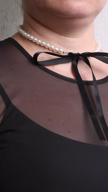 The woman makes a review of the purchase. On the neck, a necklace of white pearls with black bows, on the hand of a bracelet. Vertical video.
