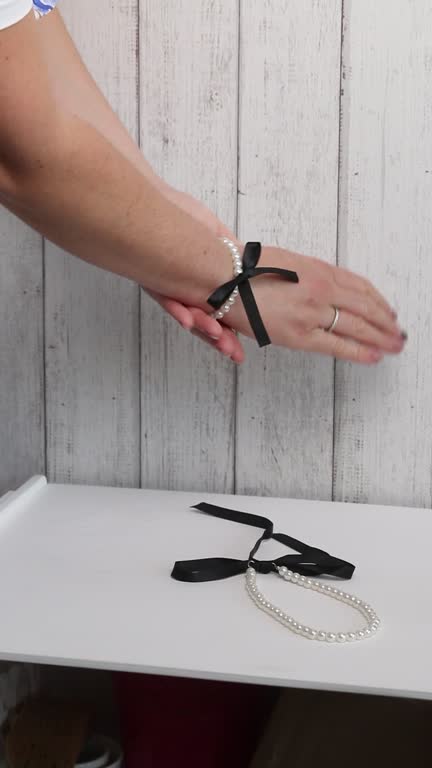 The woman makes a review of the purchase. He puts the bracelet on his hand. A necklace and white pearl bracelet with black bows. Vertical video.