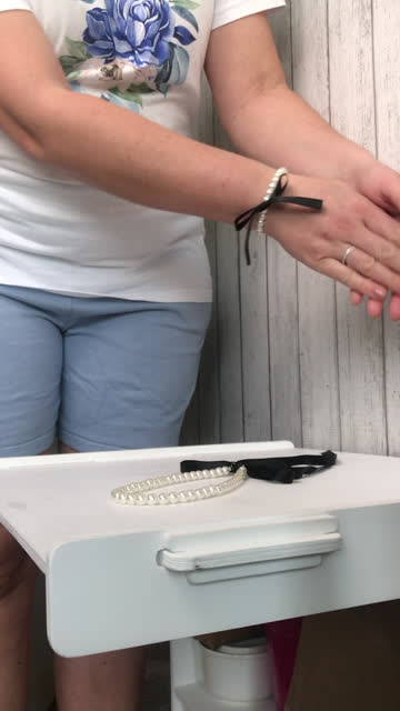 The woman makes a review of the purchase. A necklace and white pearl bracelet with black bows. He puts the bracelet on his hand. Vertical video.