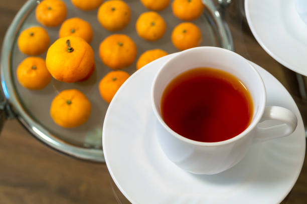 A white cup of tea sits on a white plate with a few oranges on it