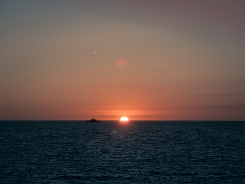 A military ship of the Spanish Navy sailing on the horizon during sunset, in Cadiz, Andalusia, Spain