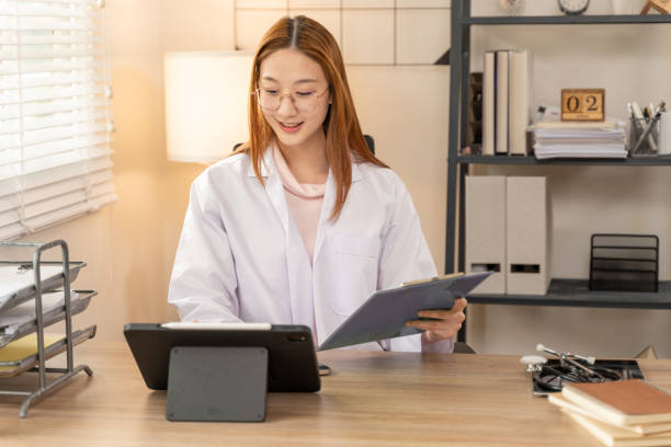 istock Happy young female doctor taking note on her computer tablet while sitting at her office desk 2143508180