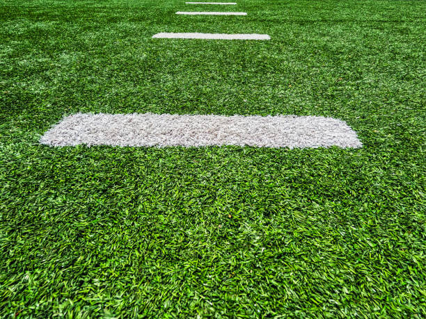 Bright green turf football field with white yard line markings. Surface level perspective.