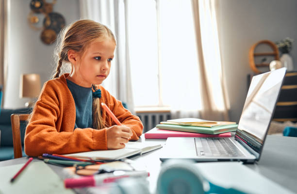 istock Learning at home. Attentive primary pupil watching recorded video lesson and making notes 2143538678