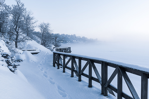 A boardwalk in Mölndal, Sweden is completely covered in snow on a chilly winter day. The white snow contrasts against the dark bridge structure, creating a striking visual scene.