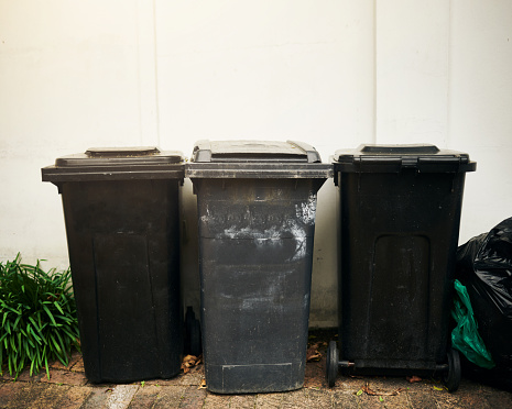 Three black rubbish bins against a white wall with copy space. Stock photo