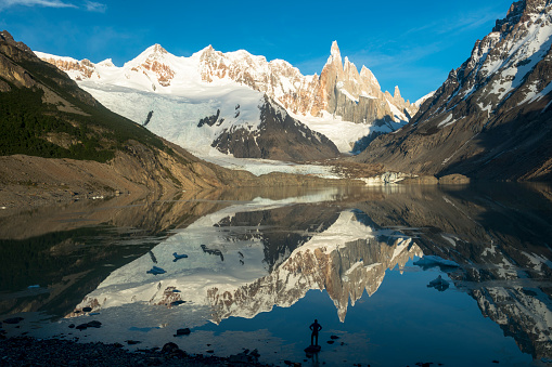 Mature hiker reflected in mountain lake with distant mountain summits, Fitzroy area, Patagonia