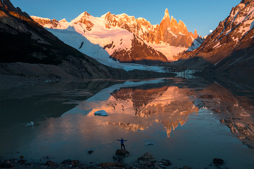 Backpacker stands on rock above lake with distant mountain summits, Fitzroy area, Patagonia