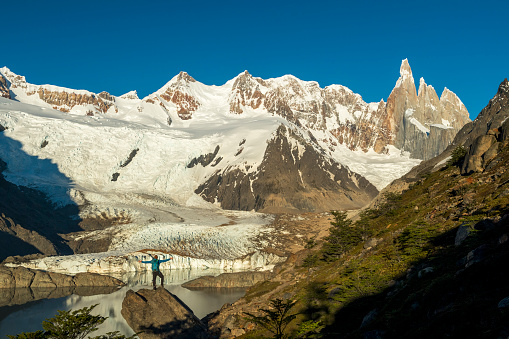 Backpacker stands on rock above lake with distant mountain summits, Fitzroy area, Patagonia