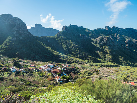 Dramatic lush green picturesque valley with old village Los Carrizales . Landscape with sharp rock formation, hills and cliffs seen from mountain road, Tenerife, Canary Islands, Spain. sunny winter day, blue sky.