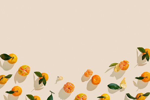 Fresh juicy orange yellow tangerines as minimal flat lay, Sweet Citrus fruits with green leaves on beige background. Top view of still life layout of mandarin oranges, above view frame, copy space