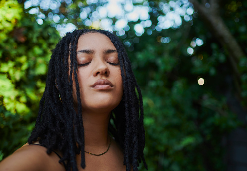 A close-up portrait of a woman with natural locks closing her eyes and taking a deep breath outdoors in nature. Stock photo